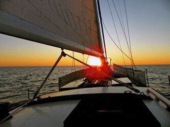 view from the stern of a sailboat heading towards sun has it sets just over the horizon