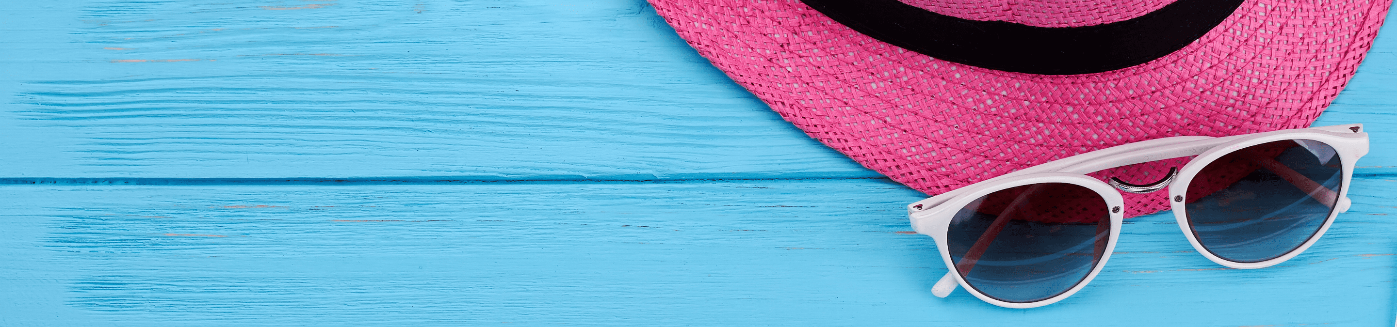 blue wooden planks with a pair of white sunglasses and a pink woven straw hat